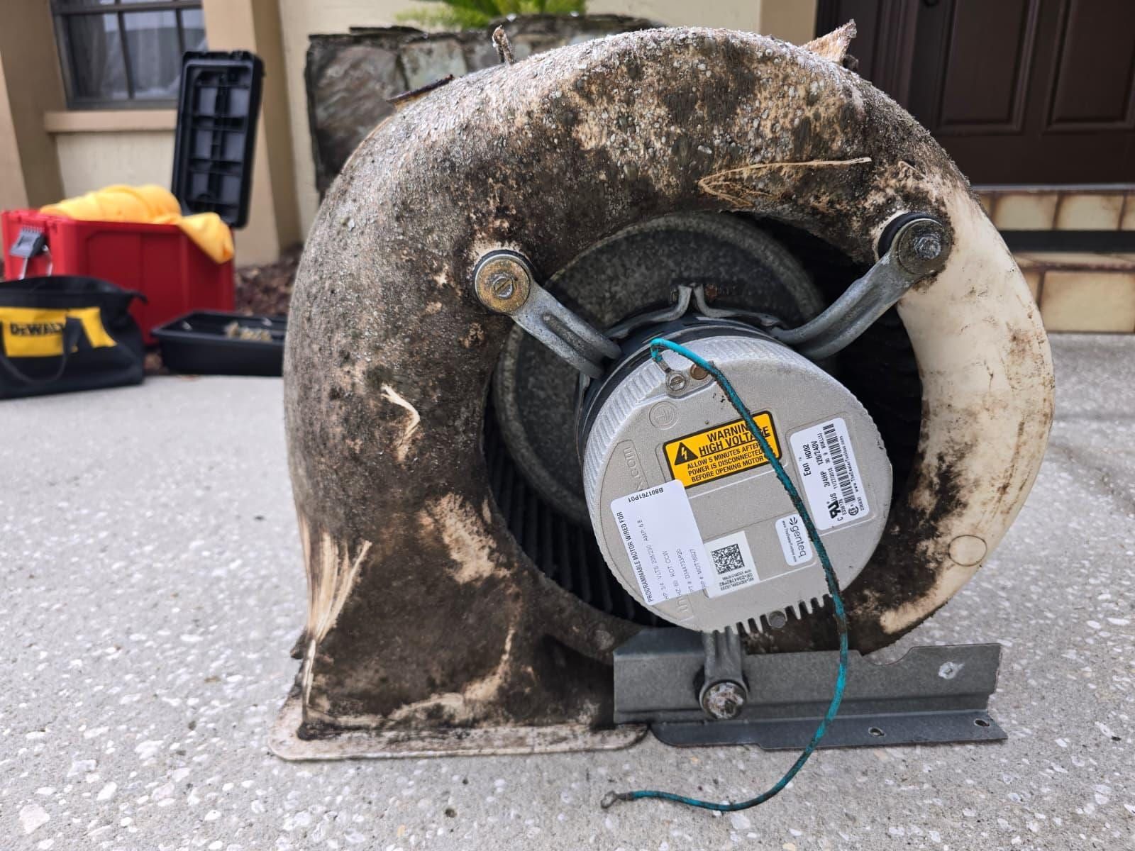 A blower wheel assembly lifted out on a driveway, its housing and blades under thick dark grime
