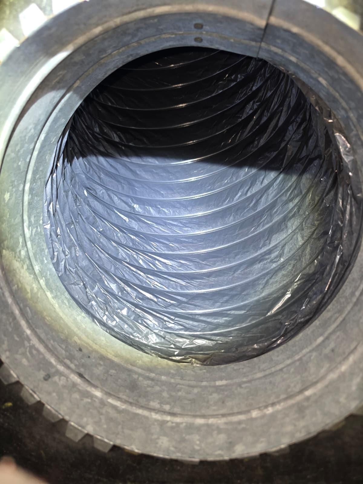 Flexible duct interior seen through a metal collar, carrying comparatively light dust