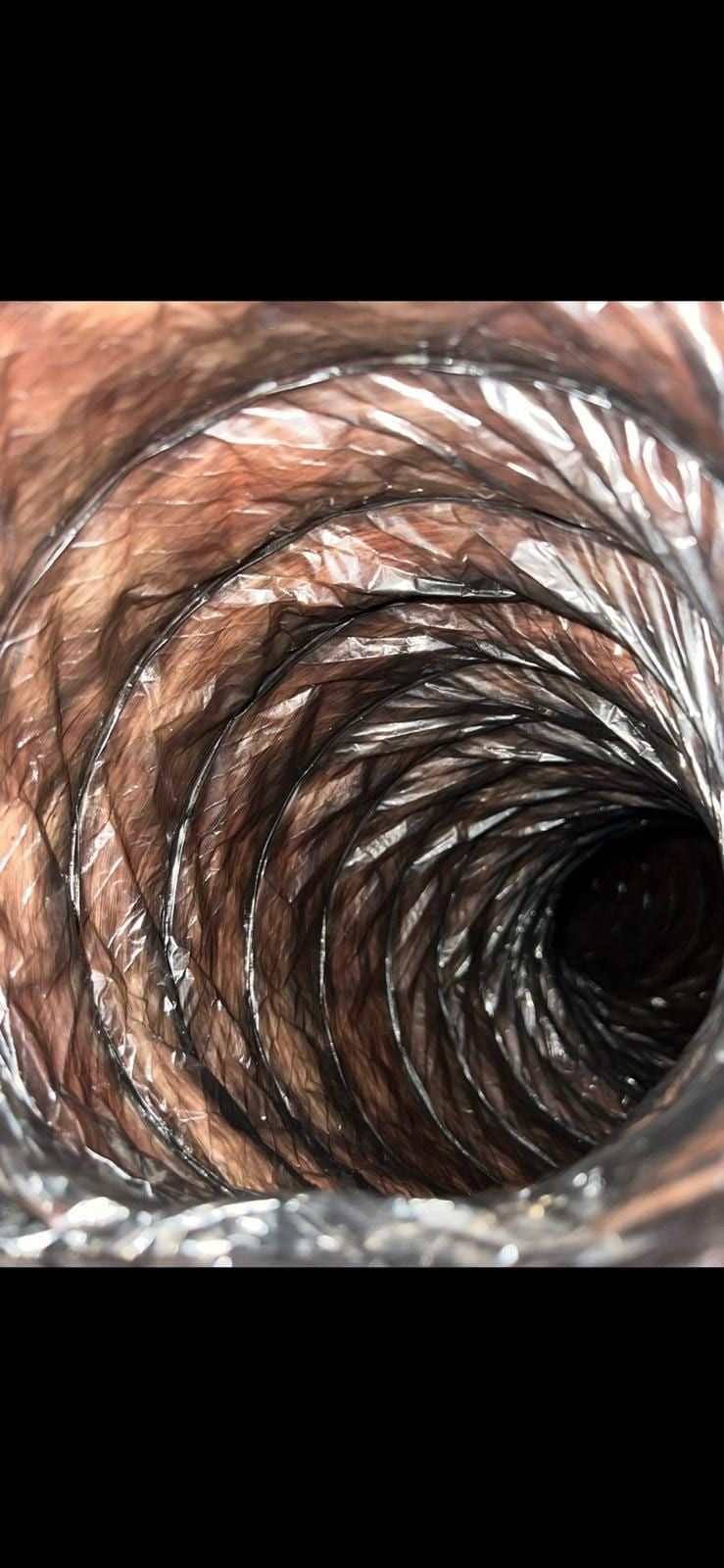 The inside of a flexible duct, its ribbed wall stained brown, tapering into darkness
