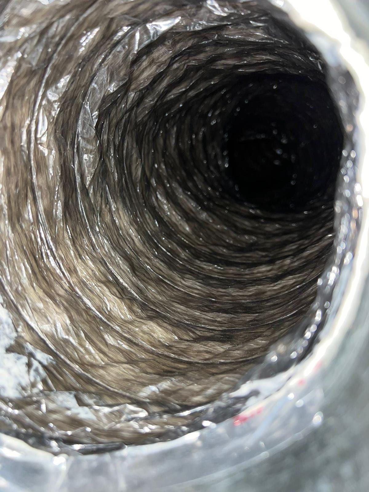 Air duct interior before cleaning, a heavy coat of grey dust packed into the spiral metal walls