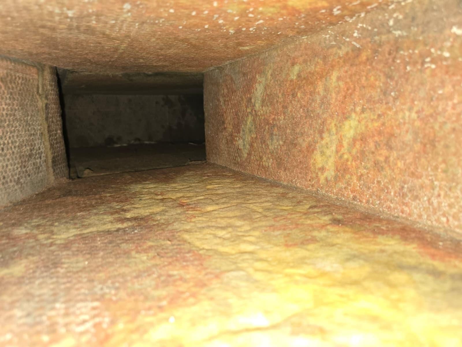 The inside of a duct board plenum, its walls stained heavy orange-brown with age