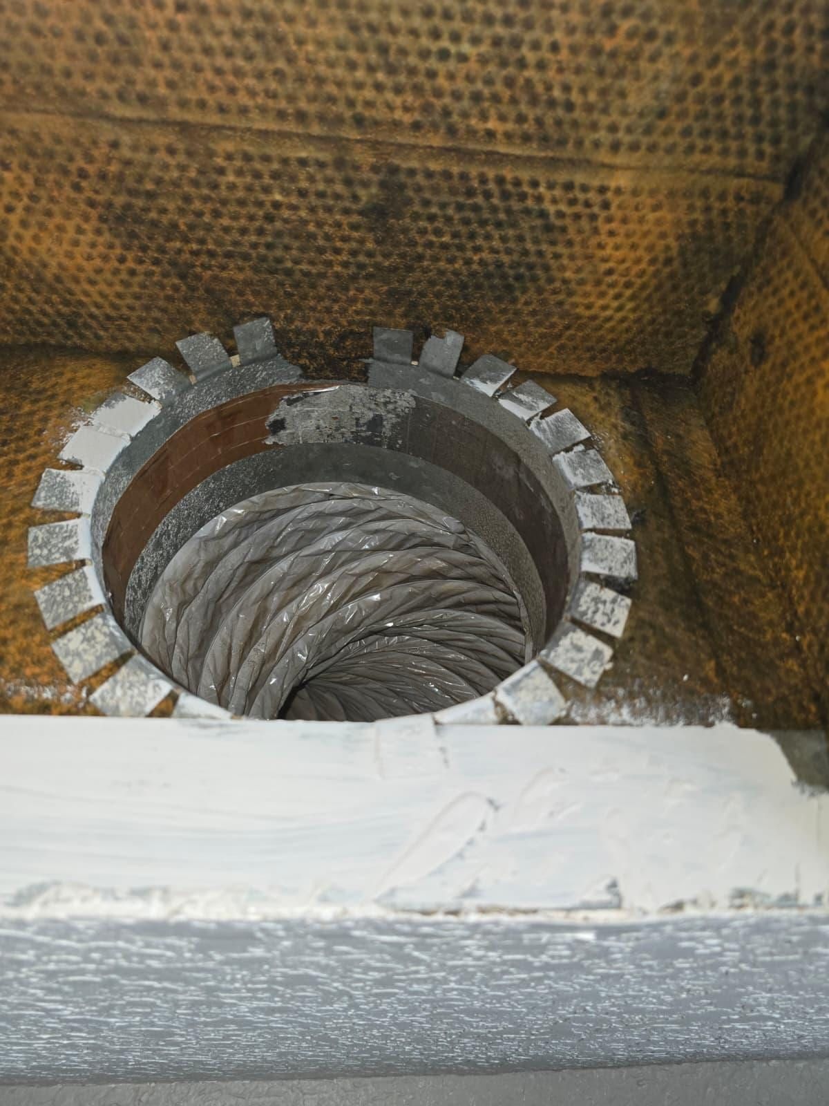 A duct board plenum stained heavy dark orange-brown, leading to a round collar with flexible duct beyond it