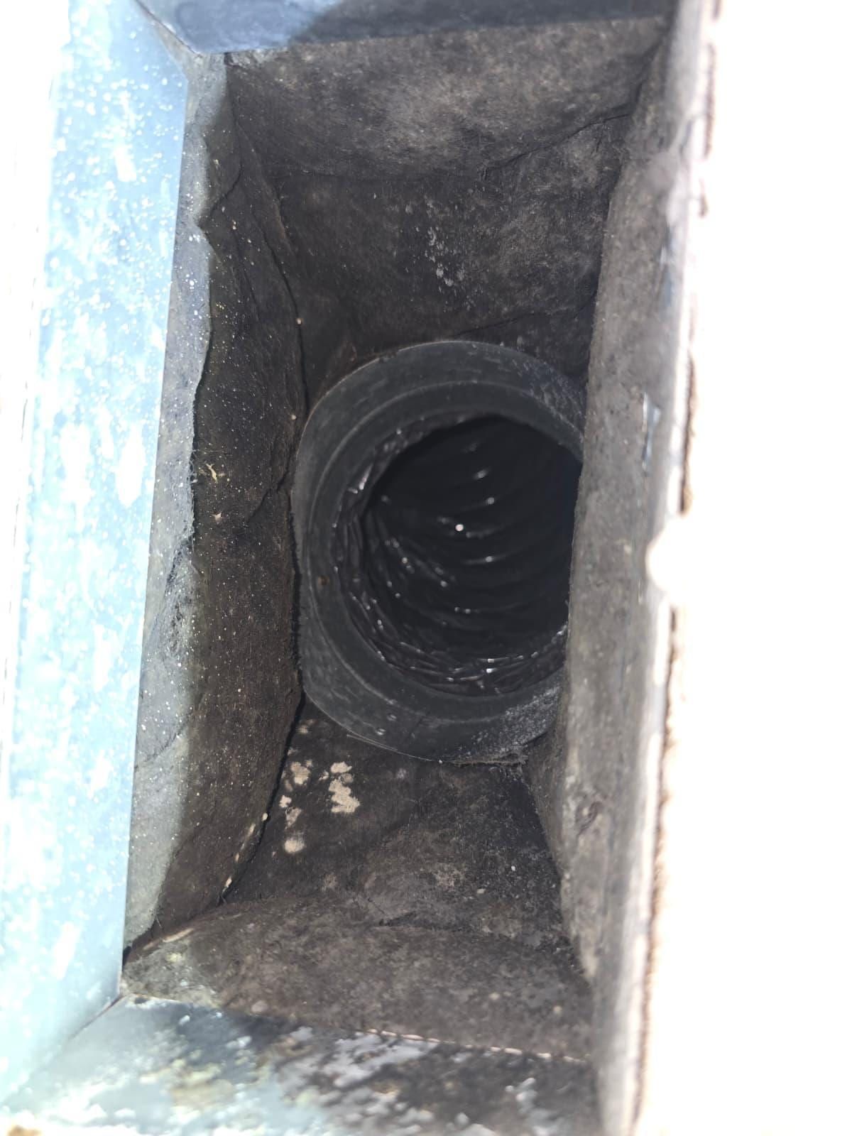 A dust-caked rectangular duct boot with a black flexible duct collar set into it