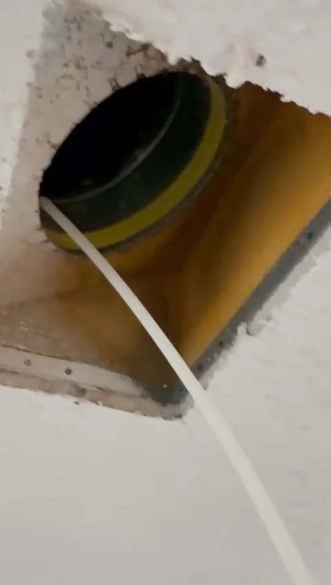 A flexible duct collar set into a ceiling boot, a supply line running off toward the frame