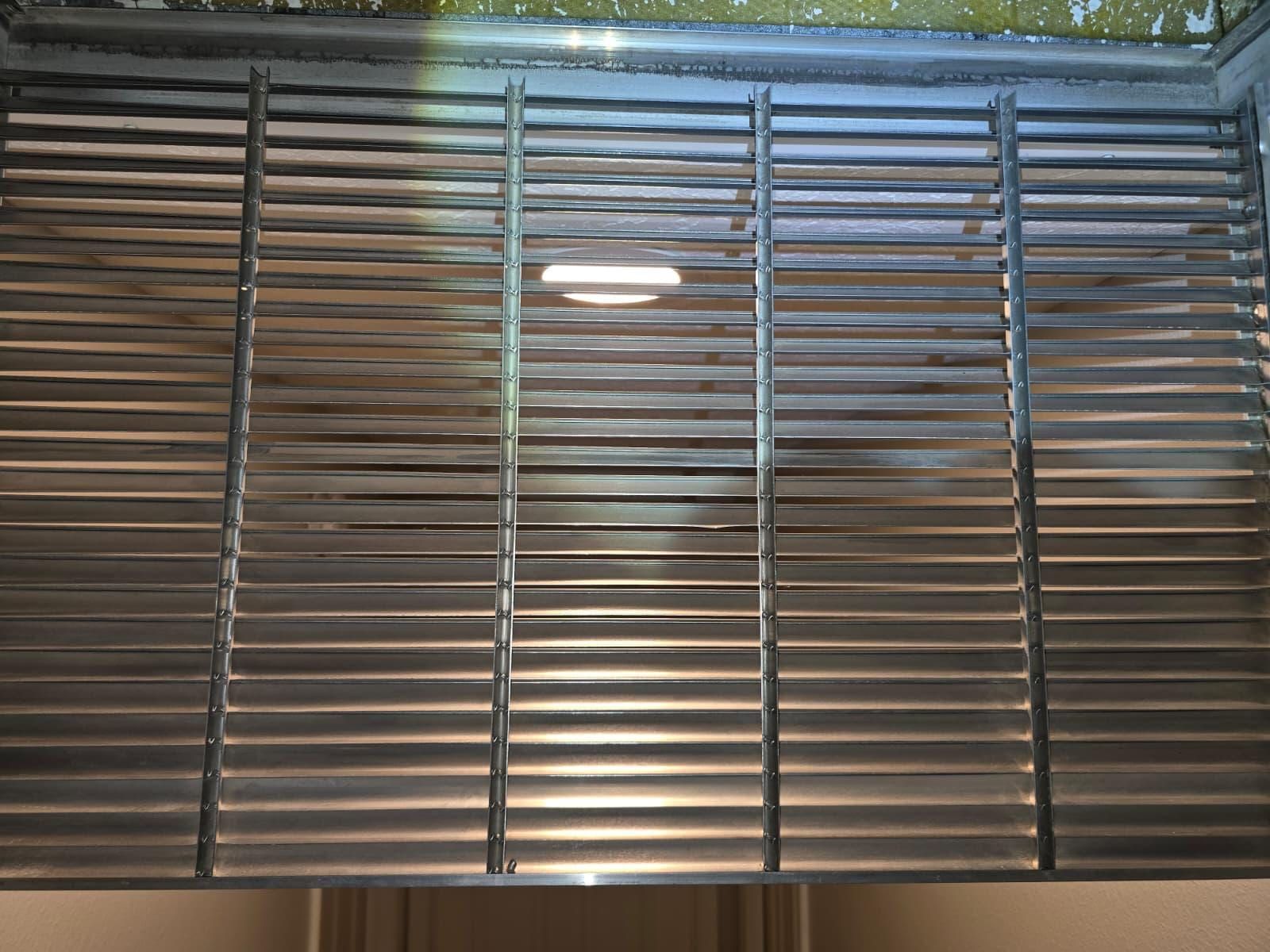 A metal return-air grille back on the wall after cleaning, its vertical louvers clear of dust