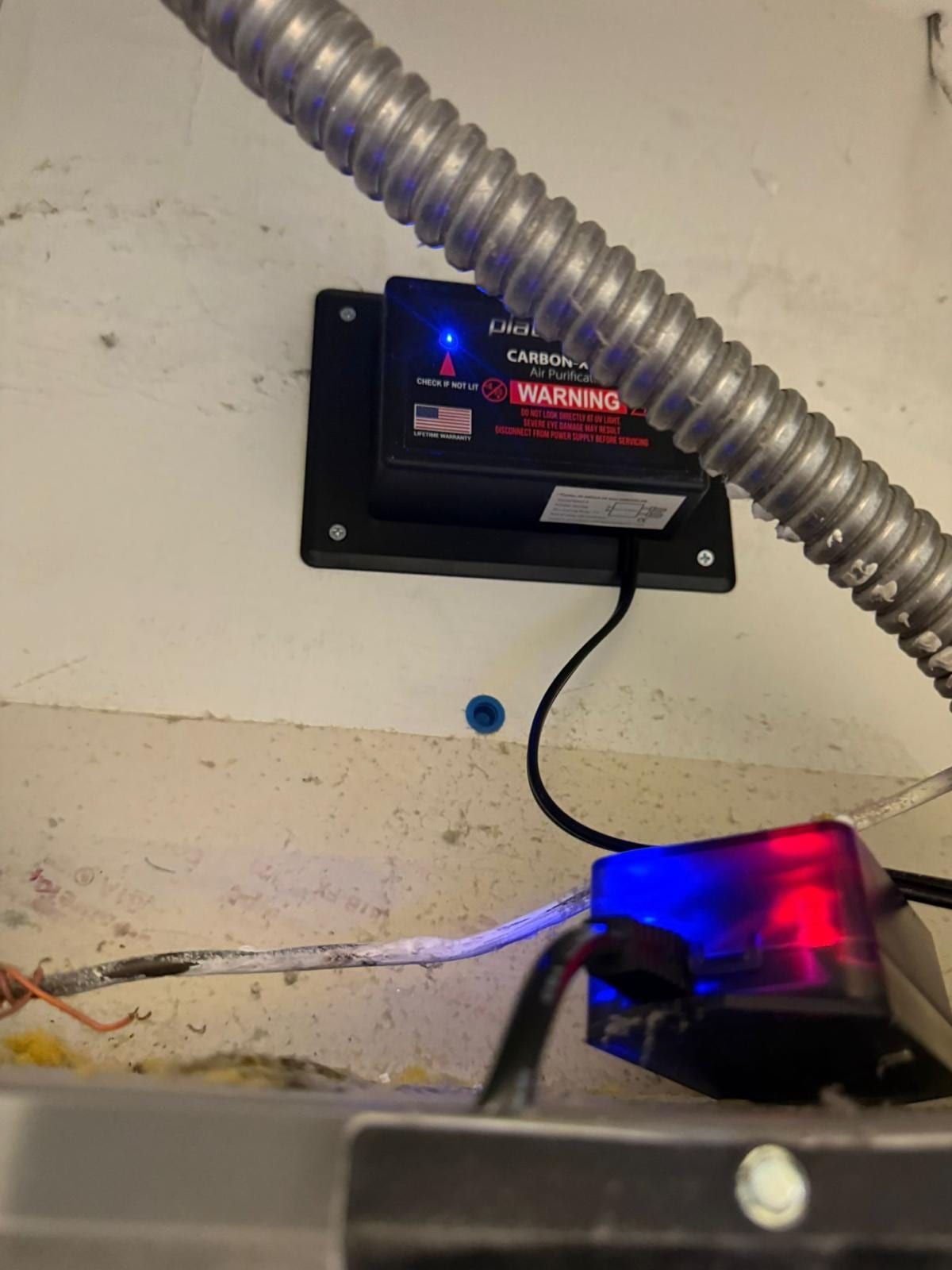 A UV air-purifier unit installed on the ductwork in a utility closet, its indicator light lit