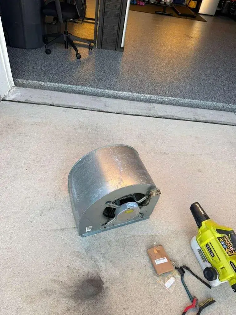 HVAC technician installing ductwork transition piece with tools on concrete floor.