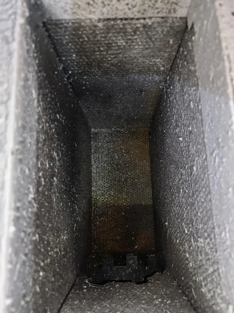 Interior view of a narrow concrete duct or pipe with accumulated dust and debris.